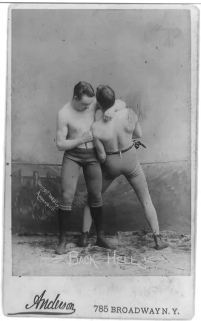 [Two men in wrestling poses in studio: back heel]