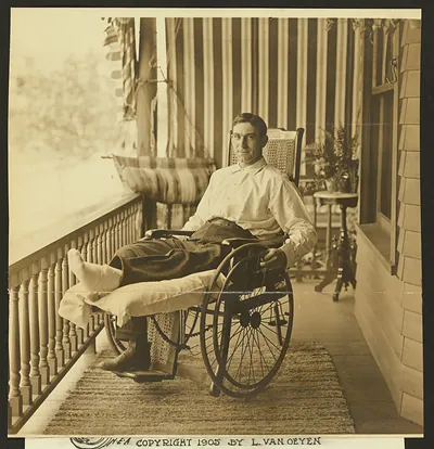 Seated man in wheelchair on a striped-awning porch