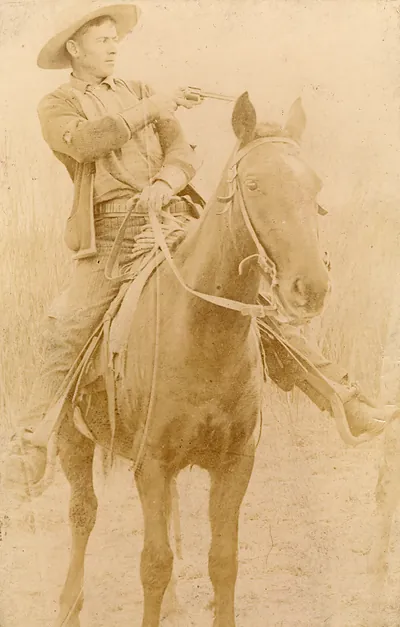 Cowboy on horseback aiming a revolver, sepia photograph