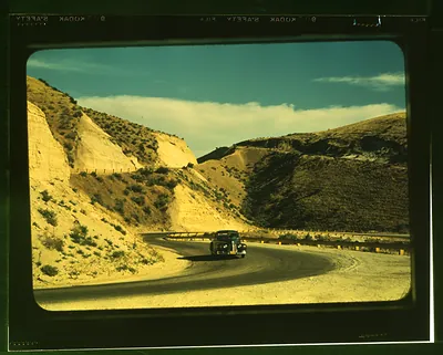 Winding road cut through dry hills, with a car