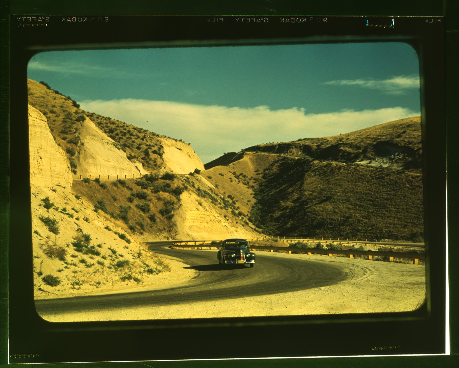 Winding road cut through dry hills, with a car — historic image
