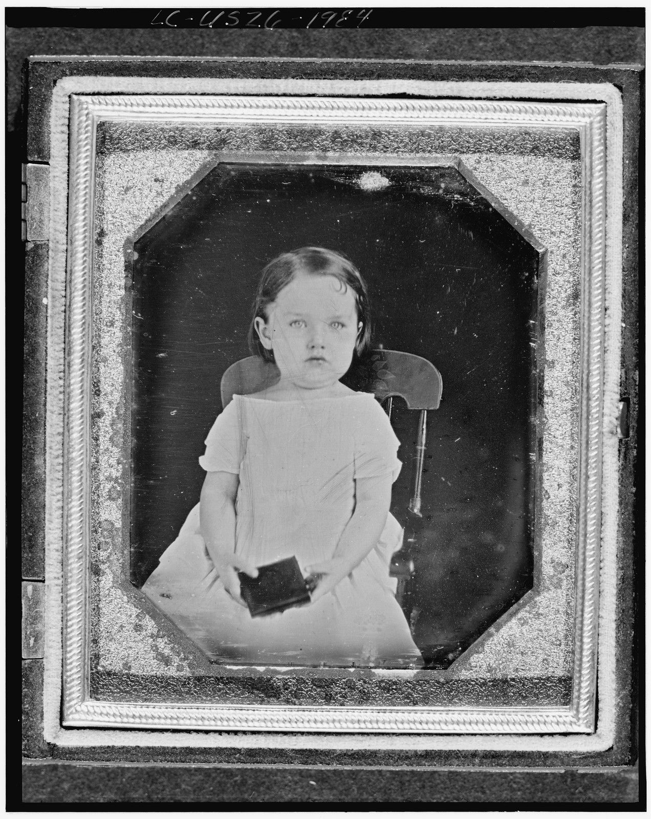 [Unidentified girl, three-quarter length portrait, facing front, seated in chair, holding a daguerreotype case(?)], [1847] — historic photograph