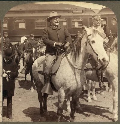 Laughing man in hat on gray horse beside a train