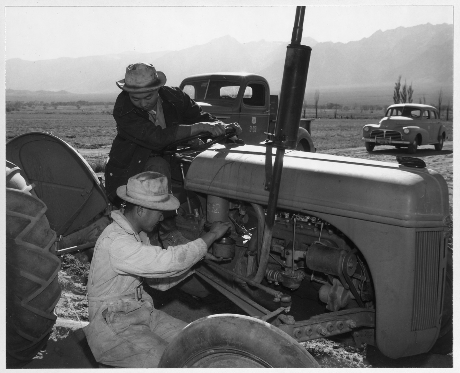 Two men working on a tractor in a field — historic image