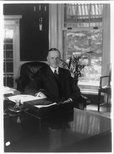 [Calvin Coolidge, half-length portrait, seated at desk in Oval Office, facing front]
