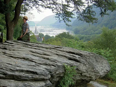 Park ranger kneeling on rock above river gorge