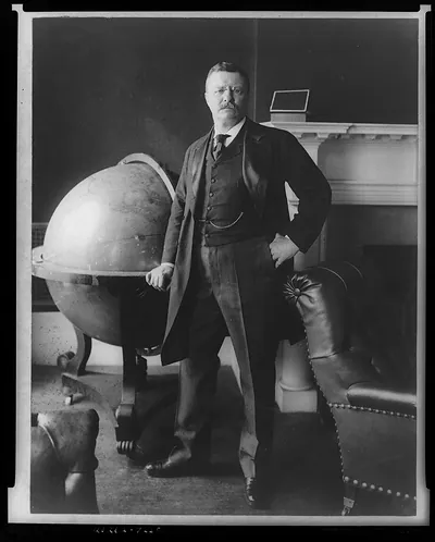 [Theodore Roosevelt, full-length portrait, standing beside large globe, facing front]