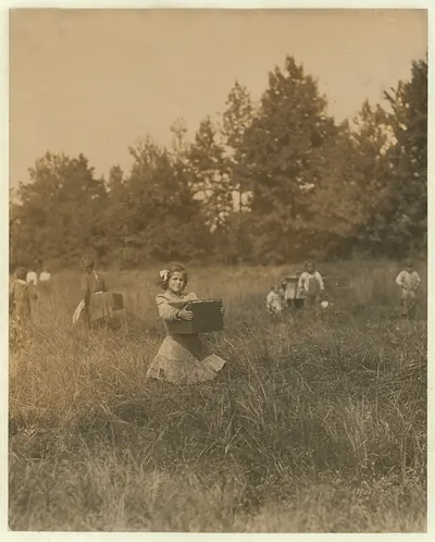 Girl carrying a box through a field with other children
