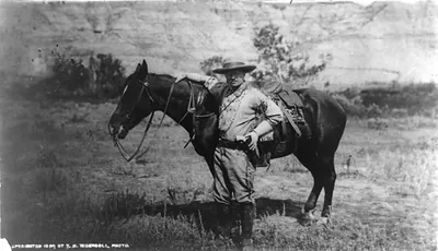 [Theodore Roosevelt, full-length portrait, standing alongside horse, facing left; wearing cowboy outfit]