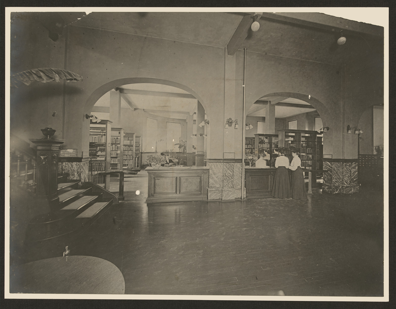 Library interior with arches, bookshelves and circulation desk — historic image