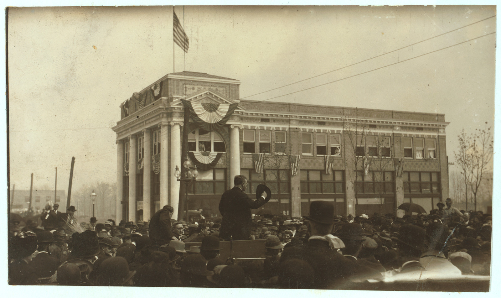 Speaker addressing a large crowd before a bunting-draped building — historic image