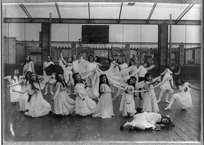 [The dance of the Children of the Sunshine with Ellen sleeping in the foreground. [#4140: Miss Mackay's Pageant Children of Sunshine and Shadow as presented at Washington Irving High School. L.W. Hine.] Location: New York, New York (State) / L.W. Hine.