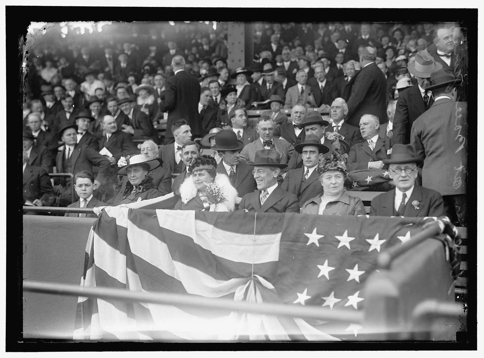 Crowd in stadium stands behind flag bunting, men and women — historic image