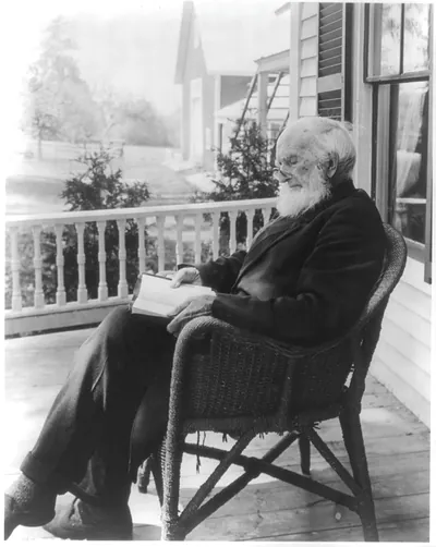 Old Man Reading Bible in Wicker Chair on Farmhouse Porch