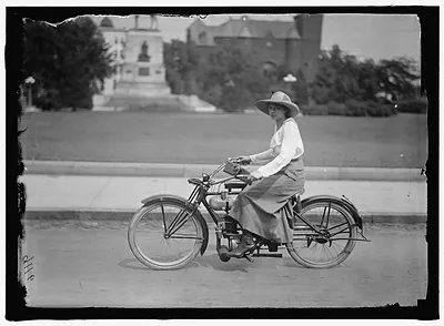 Woman in a long skirt and hat riding a motorcycle