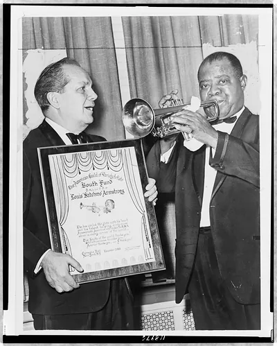[Louis Armstrong plays trumpet while Joey Adams, president of the American Guild of Variety Artists Youth Fund, presents him with an award at Carnegie Hall]