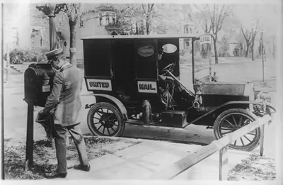 [Mailman emptying mailbox, automobile marked United Mail" at curb]"