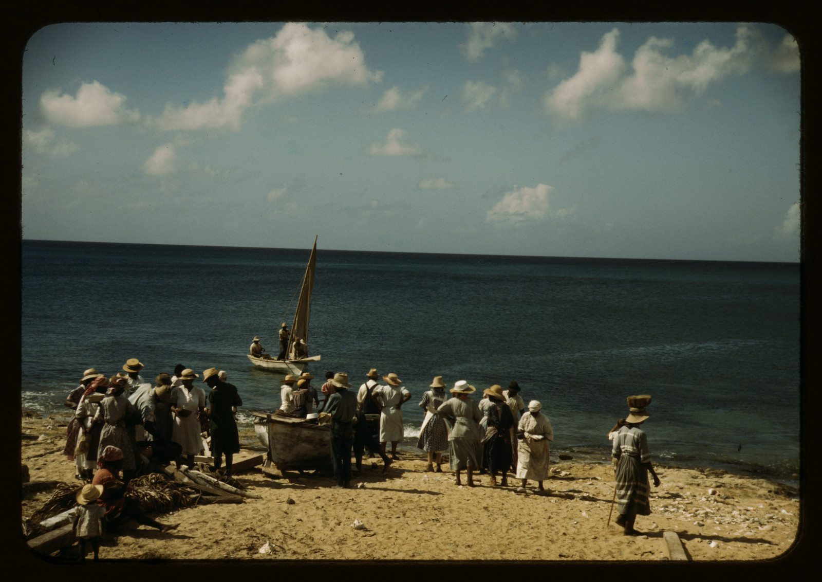 Crowd on beach beside sailboat and fishing boat — historic image