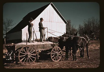 Two men on horse-drawn wagon before a barn