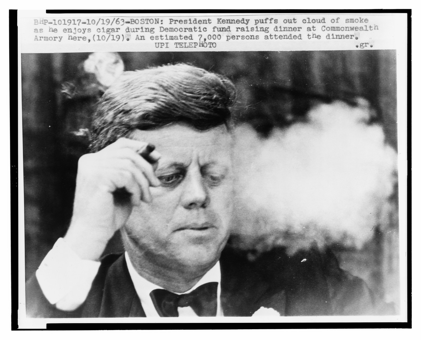 [President John F. Kennedy, head-and-shoulders portrait, smoking a small cigar at a Democratic fundraiser in Boston's Commonwealth Armory], 1963 October 19. — historic photograph
