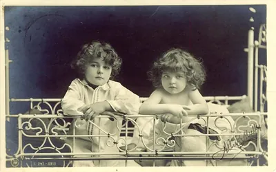 Two curly-haired children behind an ornate white iron bed rail