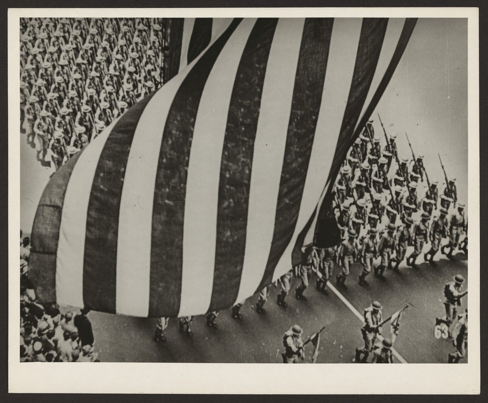 Soldiers marching beneath a giant American flag in a parade — historic image