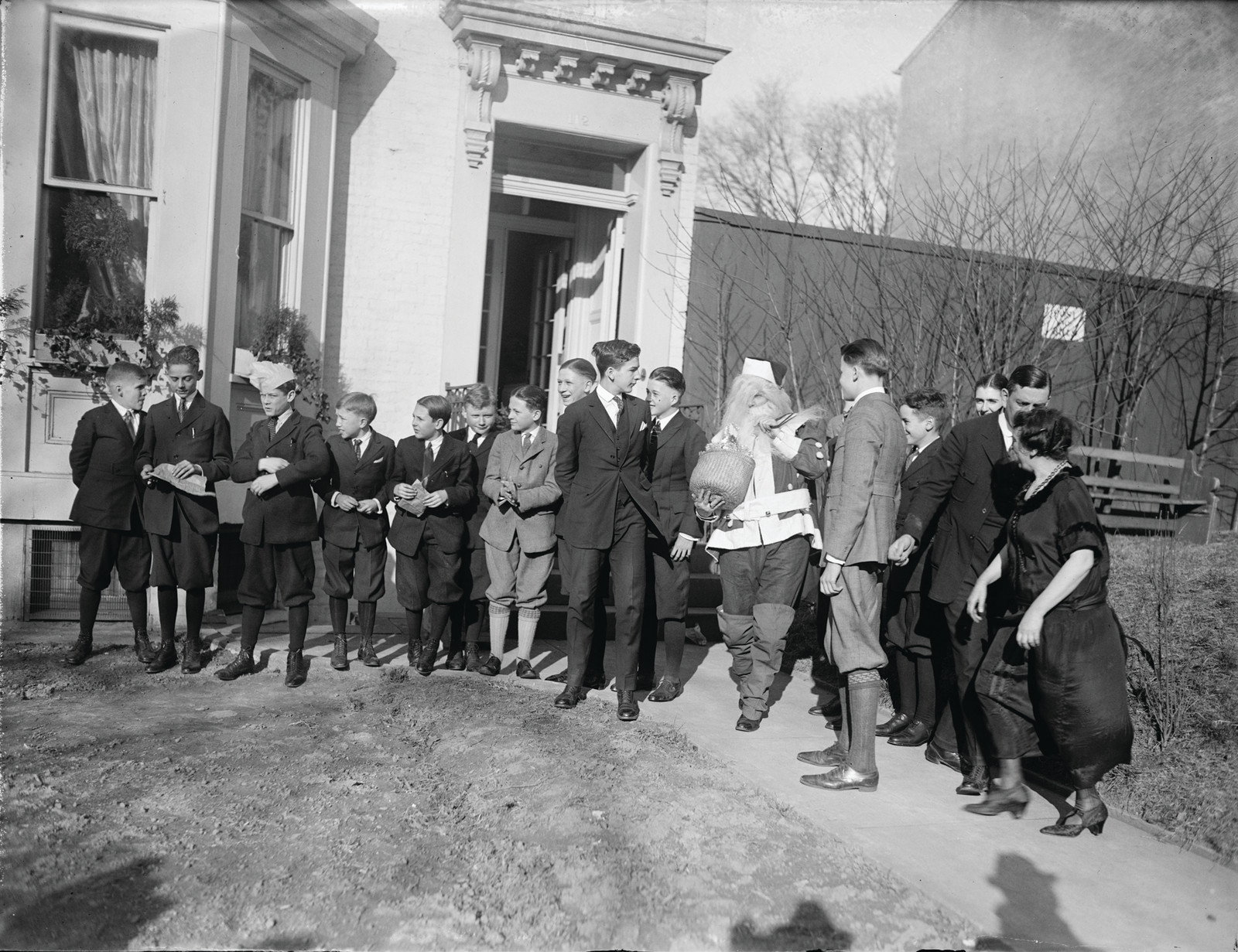 Boys gather around a Santa Claus figure outside a house — historic image