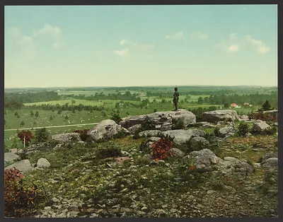 Hand-colored photograph of rocky battlefield overlook with soldier statue