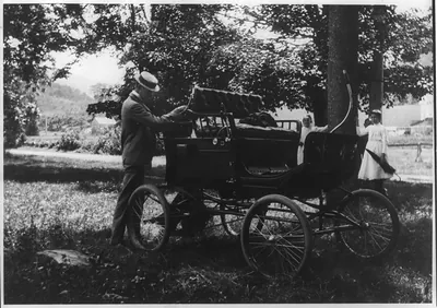 [Man standing behind early automobile]