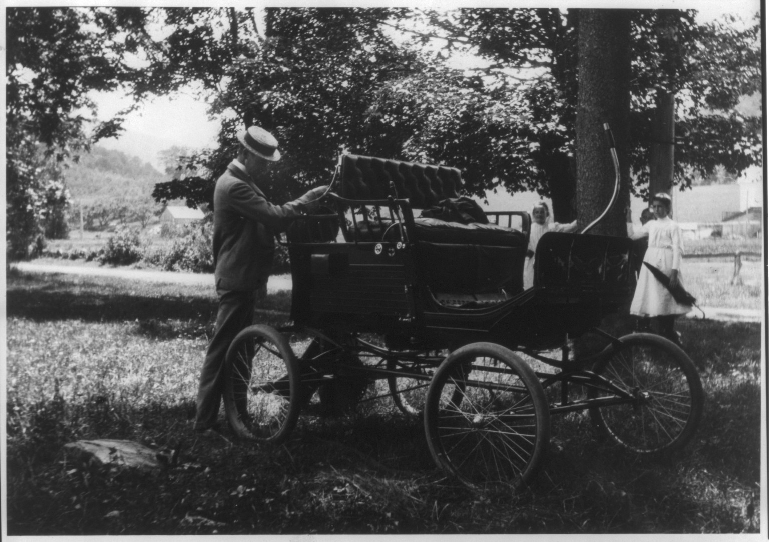 [Man standing behind early automobile] — historic photograph