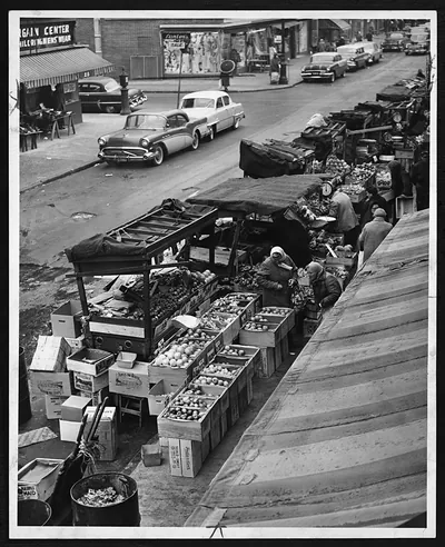 Pushcart produce market on a city street with parked cars