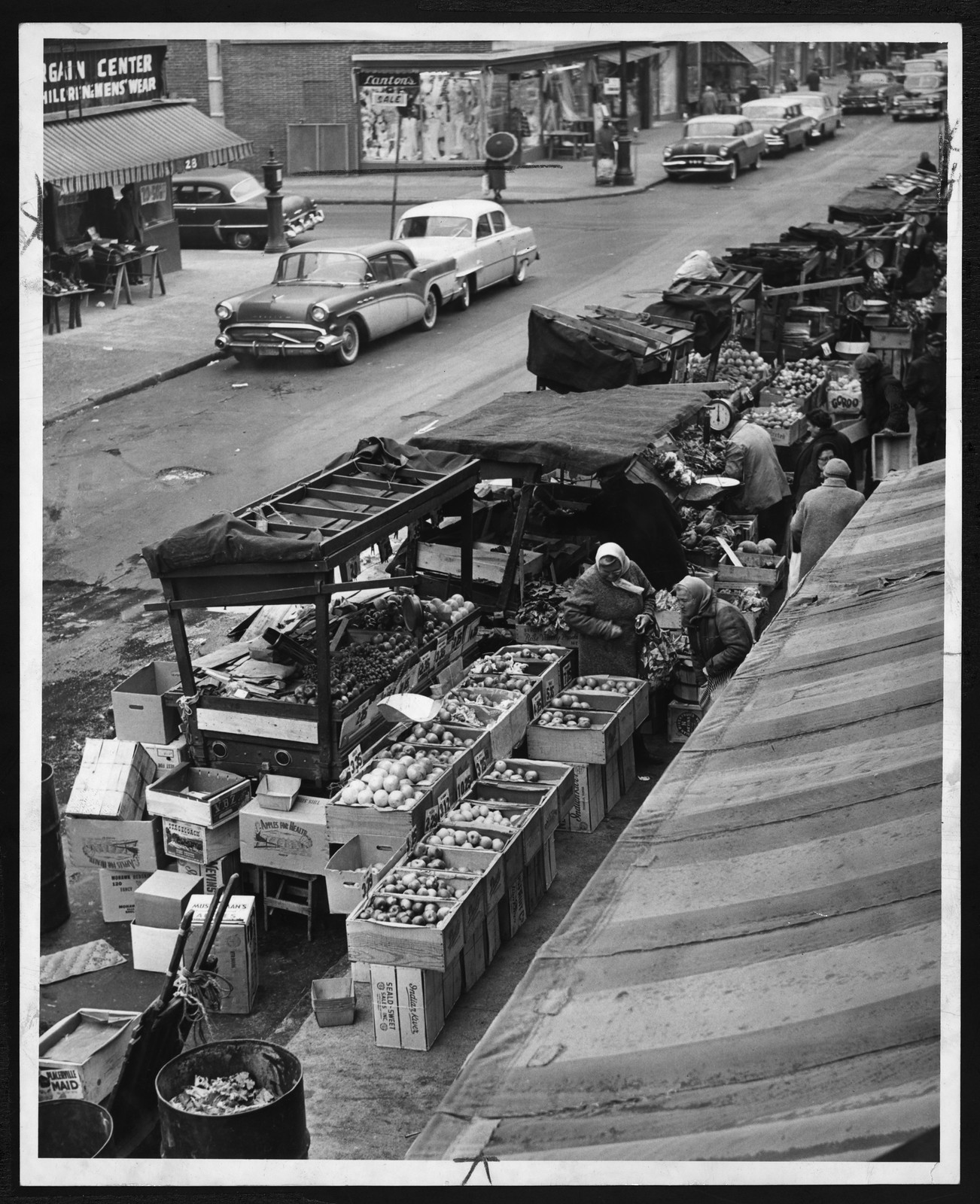 Pushcart produce market on a city street with parked cars — historic image