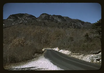 Winding mountain road beneath a rocky, wooded peak