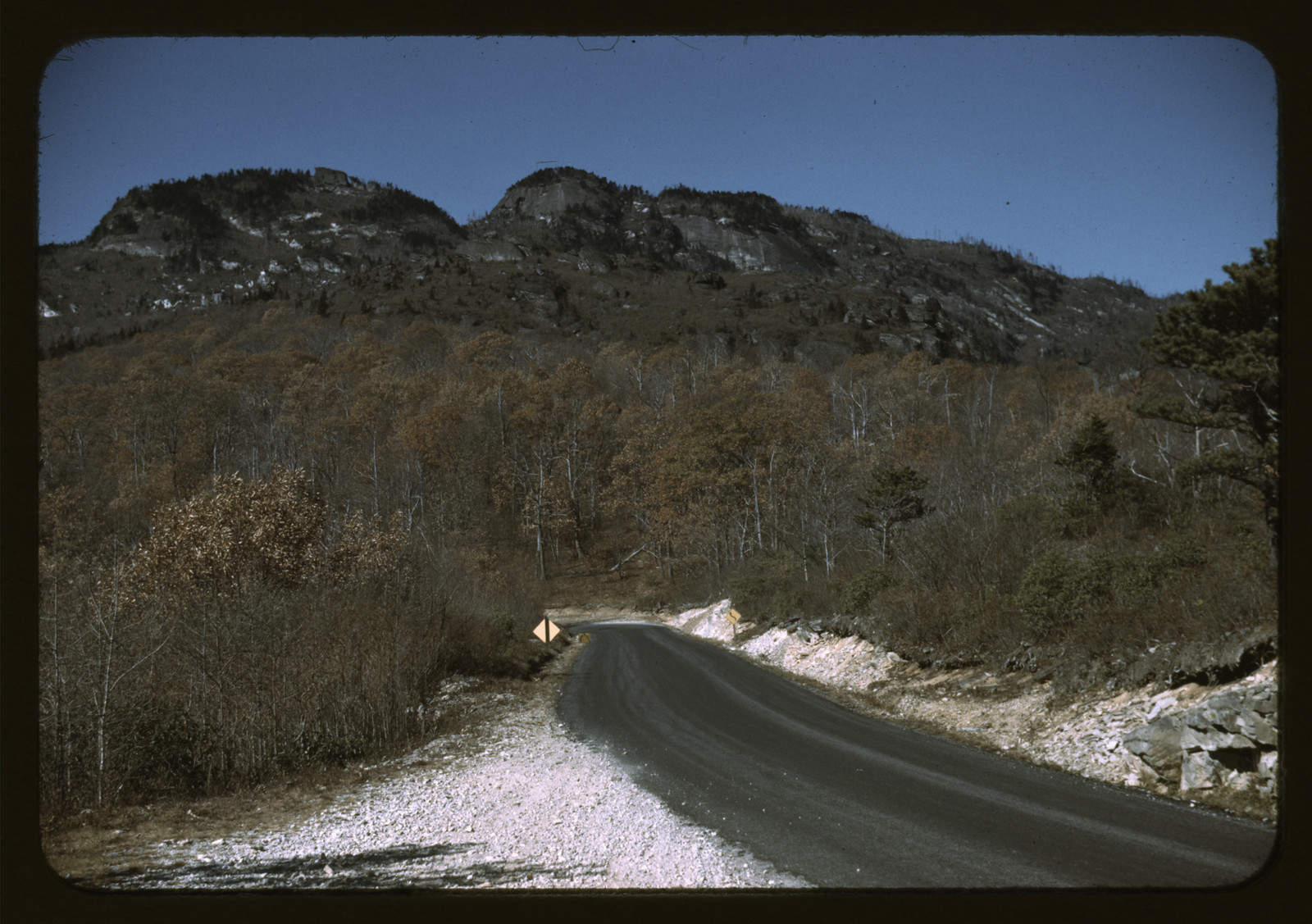 Winding mountain road beneath a rocky, wooded peak — historic image