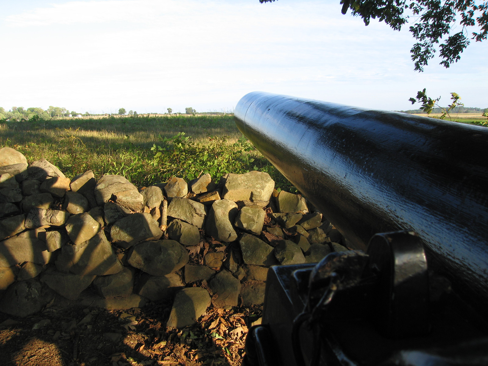 Cannon barrel pointing over stone wall, field beyond — historic image