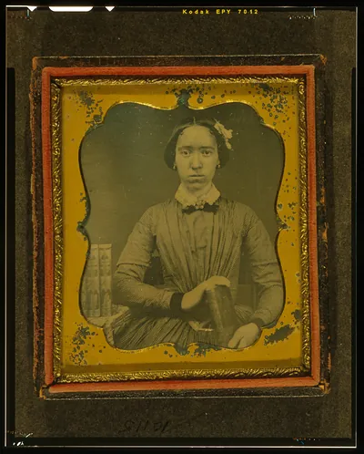 [Unidentified woman holding book, with books on table to her right]