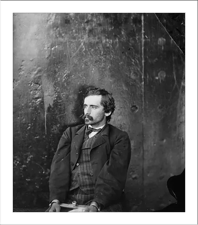 Seated man with mustache in studio portrait, metal backdrop