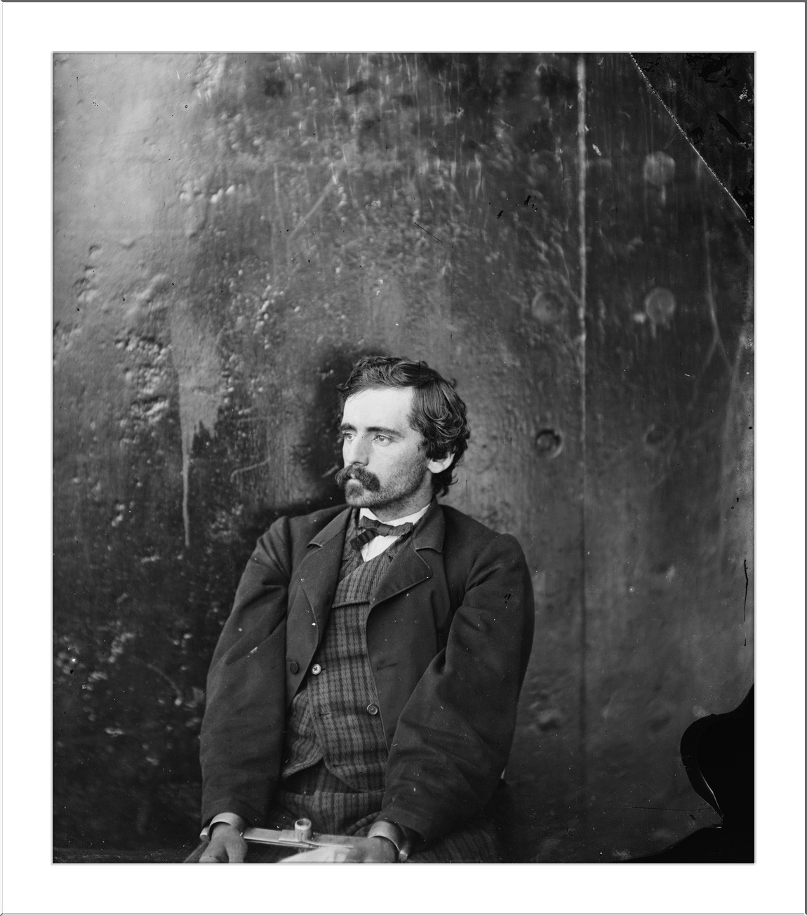 Seated man with mustache in studio portrait, metal backdrop — historic image