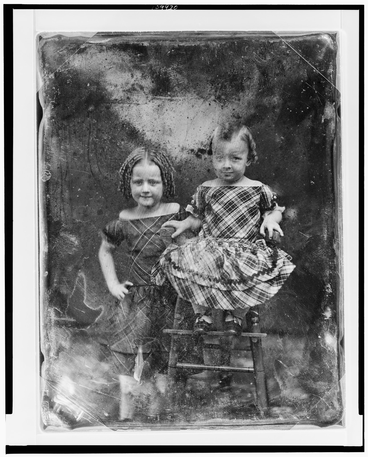 [Two unidentified girls, about three and five years of age, the younger child seated in high chair, older one standing beside her on left, both nearly facing front], [between 1844 and 1860] — historic photograph
