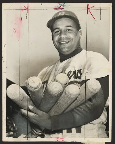 Smiling baseball player holding several bats, photograph