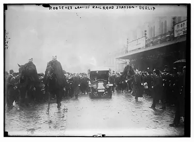 Roosevelt leaving railroad station Berlin. Crowd, car, and men on horseback.