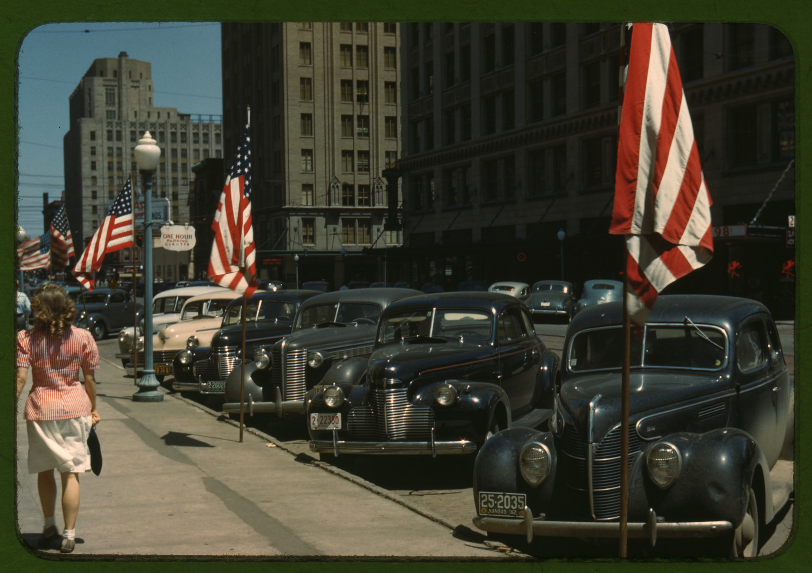 1940s city street with parked cars and American flags — historic image