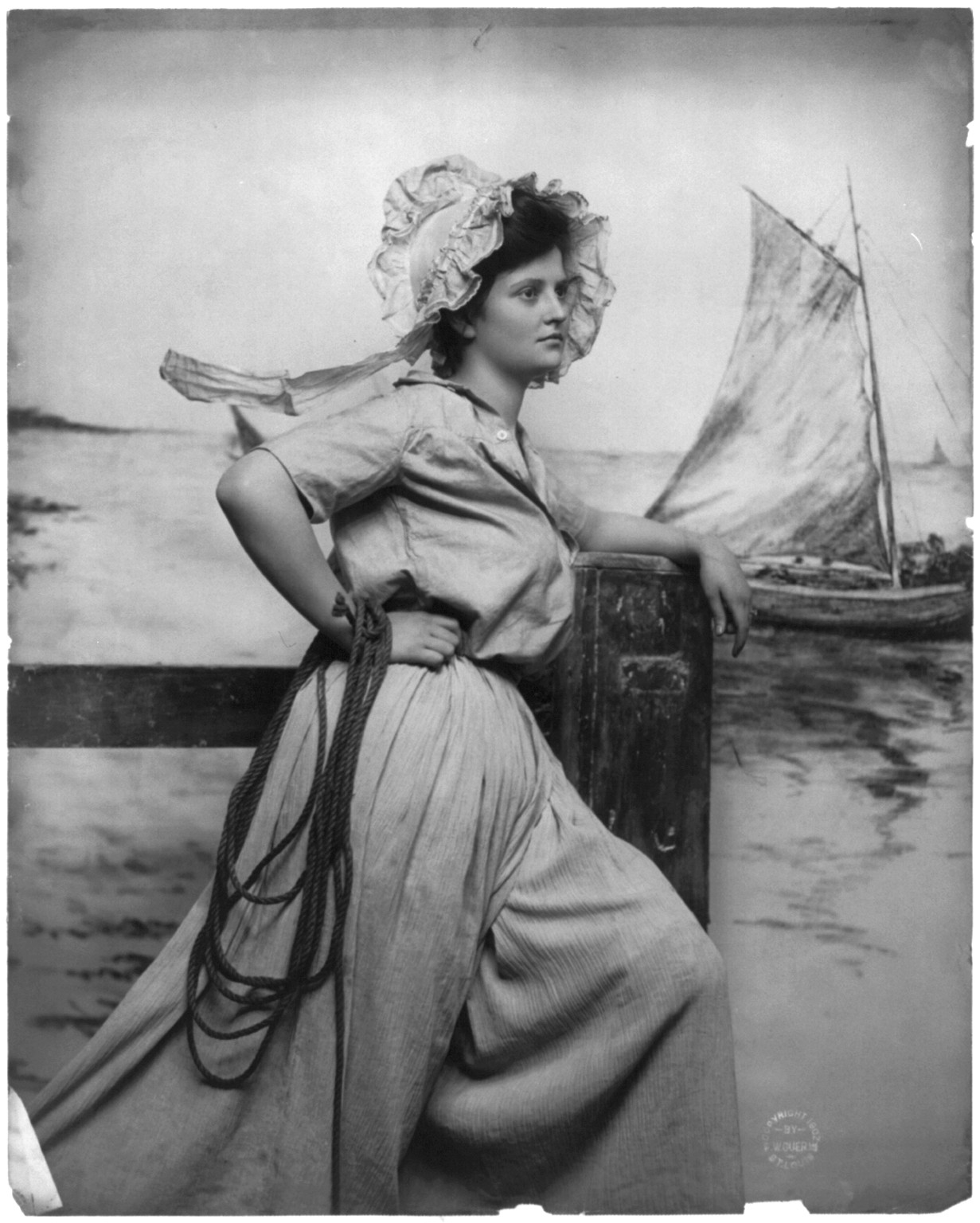 [Woman wearing bonnet, holding rope and standing on pier; fishing boat in background], c1902. — historic photograph