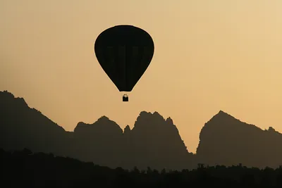Hot air balloon silhouetted against sunset mountains