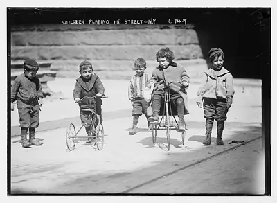 Children with tricycles, playing in street, New York