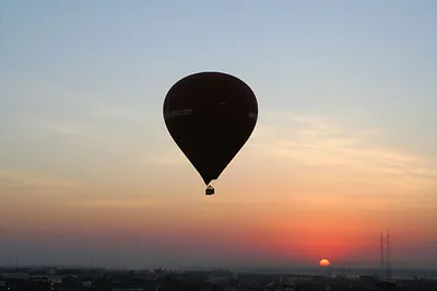 Hot air balloon silhouetted against a sunrise over a city