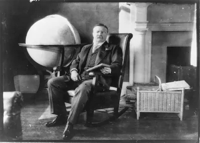 [Theodore Roosevelt, full-length portrait, seated by globe and mantle, facing slightly right, holding book]