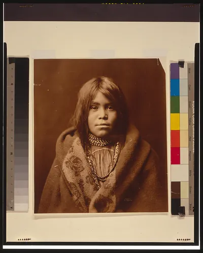 [An Apache girl, head-and-shoulders portrait, facing front, wearing bead necklace, with blanket around her]