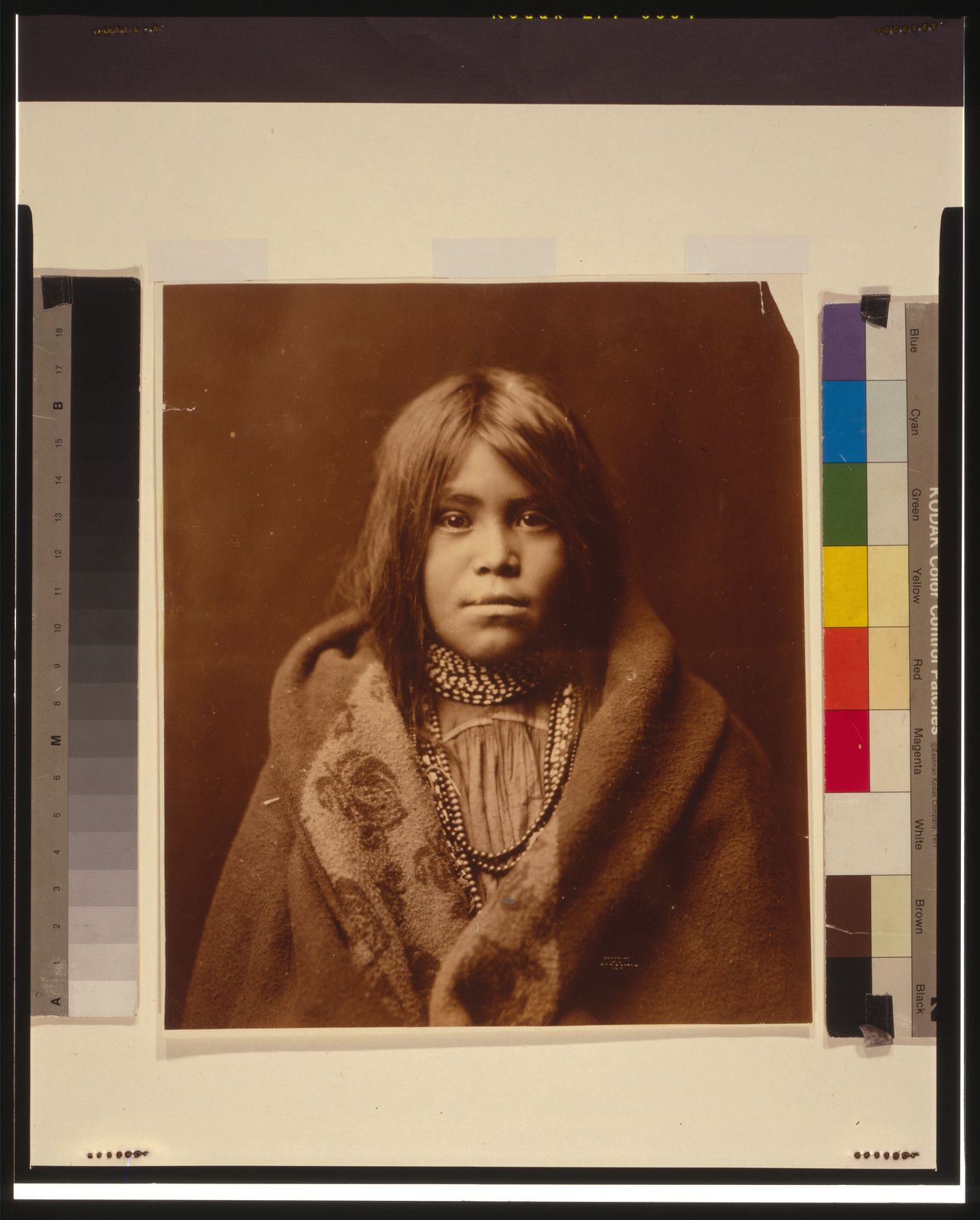 [An Apache girl, head-and-shoulders portrait, facing front, wearing bead necklace, with blanket around her], c1903. — historic photograph