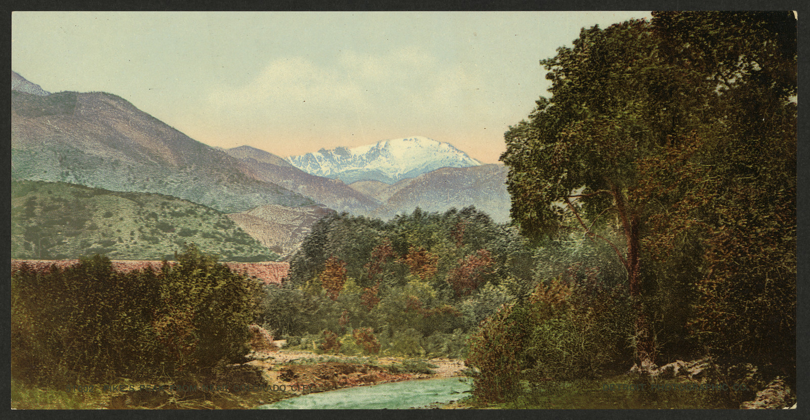 Snow-capped mountain peak above a wooded river valley — historic image